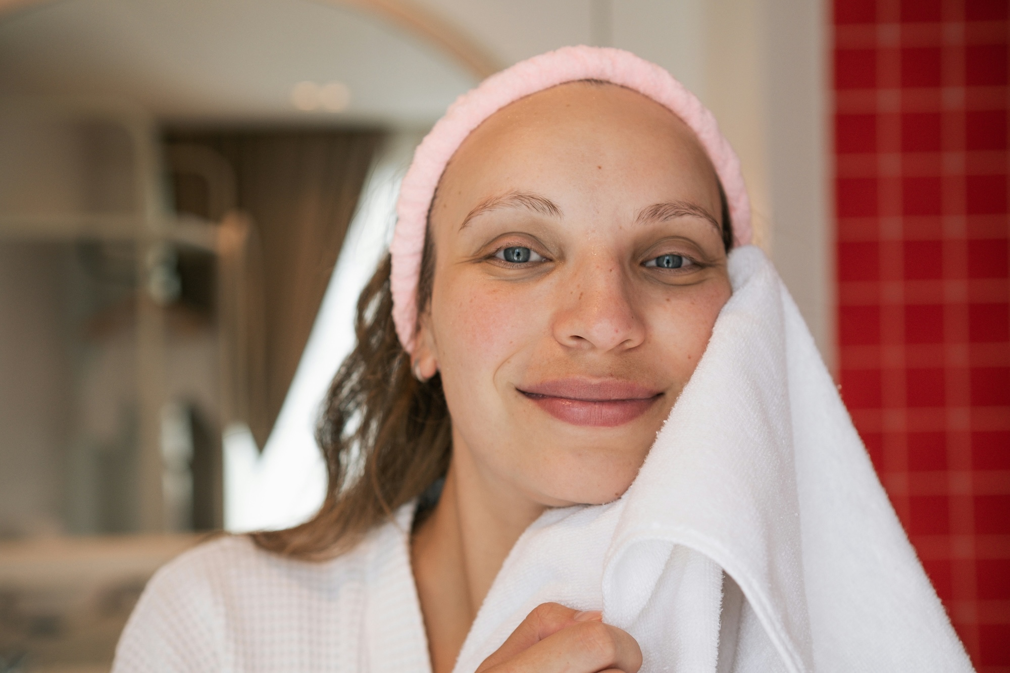 After her Venus Legacy facial treatment in St. Charles, IL, a woman in a robe presses a soft towel to her cheek as she follow proper post-treatment care.